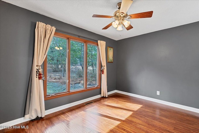 unfurnished room with visible vents, a textured ceiling, baseboards, and wood finished floors