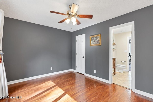 unfurnished bedroom with a textured ceiling, connected bathroom, wood finished floors, a ceiling fan, and baseboards