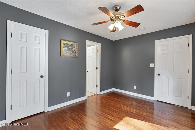 unfurnished bedroom featuring a textured ceiling, dark wood-style flooring, a ceiling fan, and baseboards