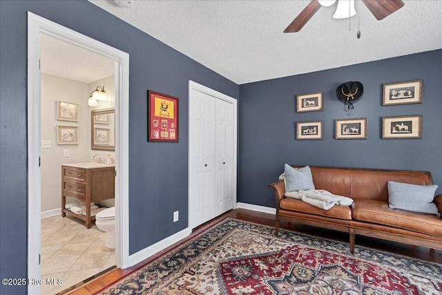 living area with a ceiling fan, a textured ceiling, and baseboards