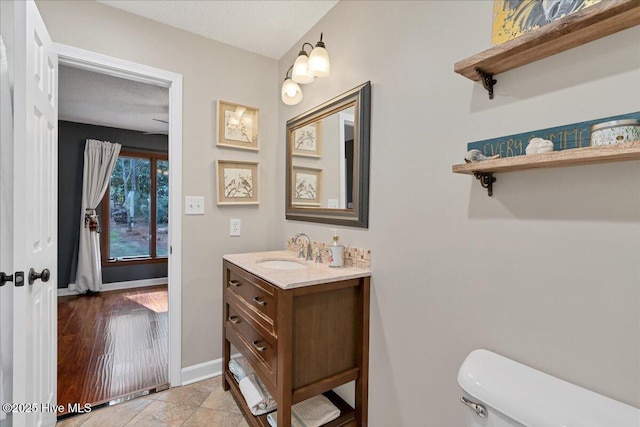 bathroom featuring a textured ceiling, toilet, vanity, and baseboards