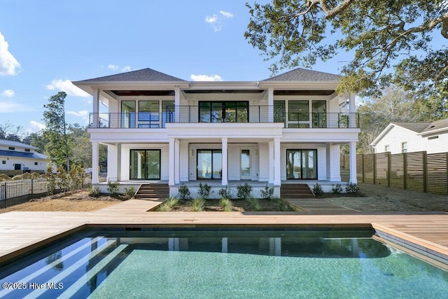 rear view of house featuring a balcony, fence, a fenced in pool, and a shingled roof