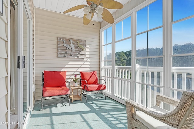 sunroom with a ceiling fan and a wooded view