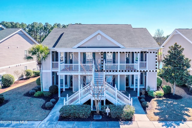 view of front facade featuring covered porch, a shingled roof, and stairway