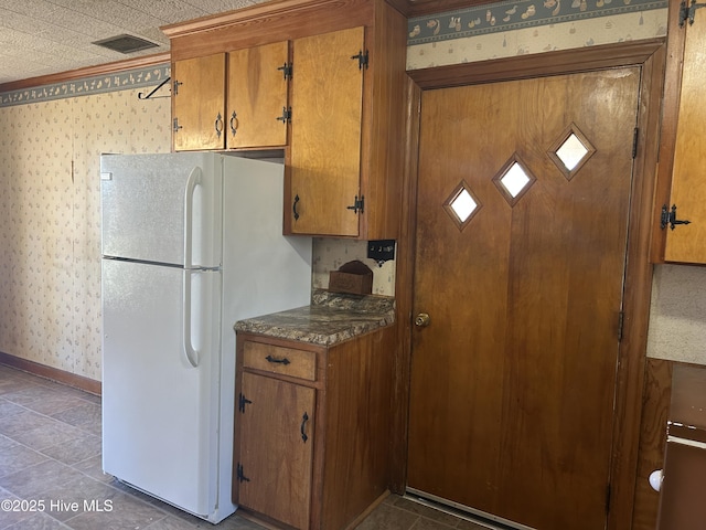 kitchen featuring freestanding refrigerator, brown cabinets, dark countertops, and wallpapered walls