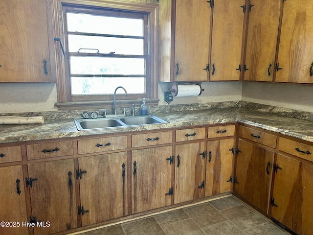 kitchen featuring brown cabinetry, dark countertops, a sink, and stone finish floor