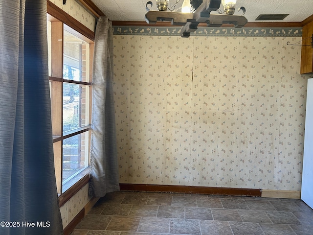 spare room featuring stone finish flooring, baseboards, and wallpapered walls