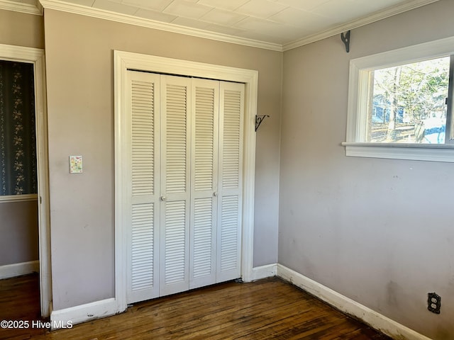 unfurnished bedroom featuring dark wood-style floors, a closet, crown molding, and baseboards