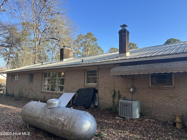 rear view of house featuring central air condition unit, a chimney, metal roof, and brick siding