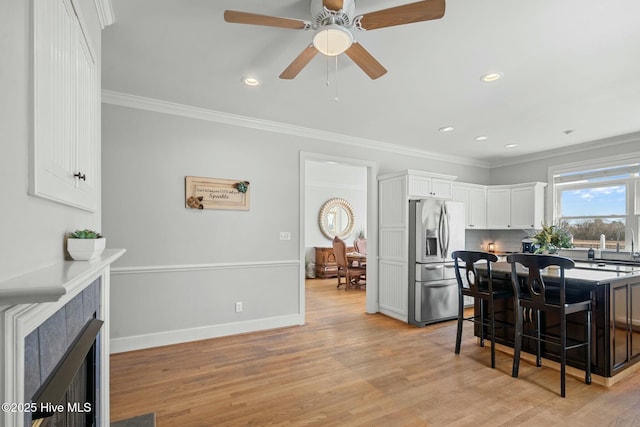 kitchen with a breakfast bar area, dark countertops, a fireplace with flush hearth, white cabinetry, and stainless steel fridge