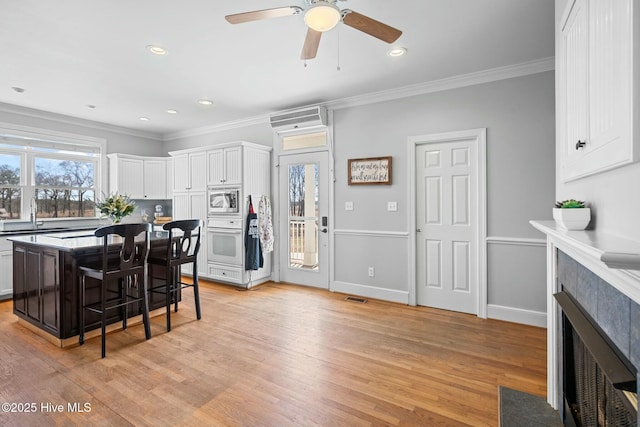 kitchen featuring a kitchen island, stainless steel microwave, a kitchen breakfast bar, oven, and white cabinetry