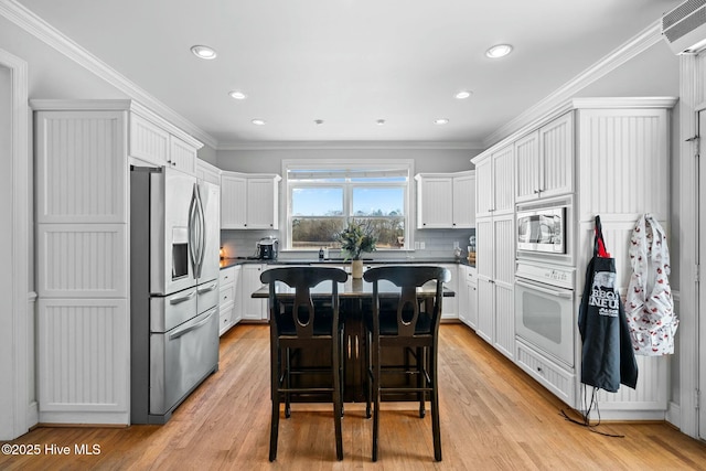 kitchen with a breakfast bar area, dark countertops, appliances with stainless steel finishes, ornamental molding, and white cabinetry