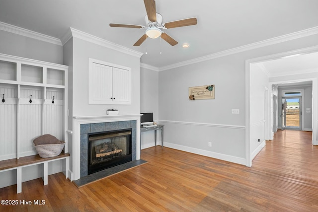 interior space with crown molding, a tiled fireplace, baseboards, and wood finished floors