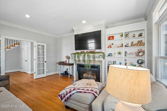 living area with wood finished floors, baseboards, stairway, a glass covered fireplace, and crown molding