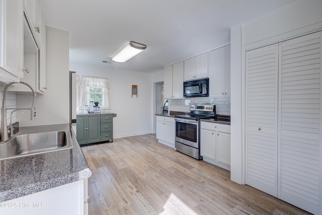 kitchen with a sink, black microwave, decorative backsplash, white cabinets, and stainless steel range with electric cooktop
