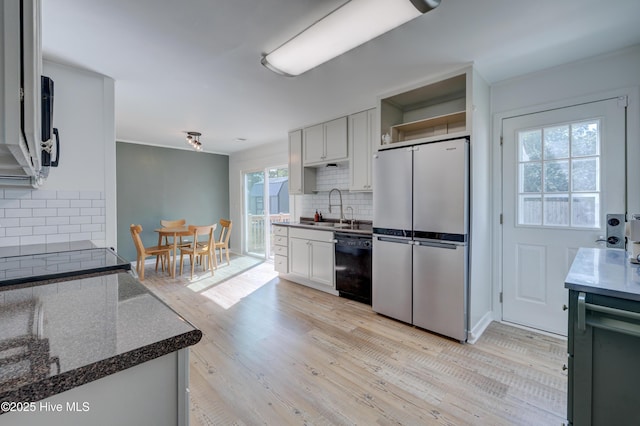 kitchen featuring a sink, freestanding refrigerator, dishwasher, backsplash, and light wood-style floors