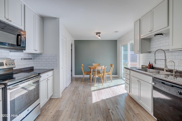 kitchen with a sink, decorative backsplash, black appliances, dark countertops, and light wood-type flooring