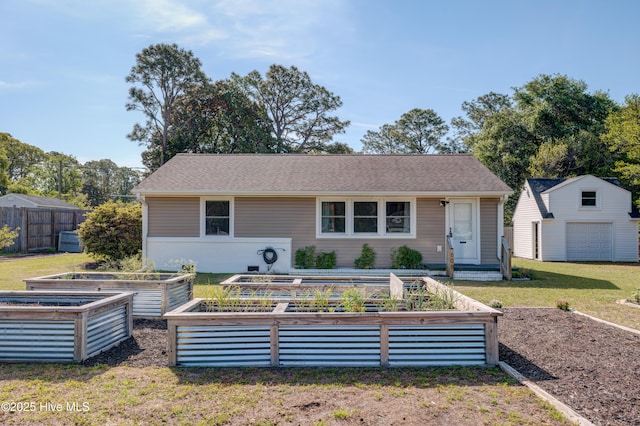 view of front facade featuring fence, a front lawn, a garden, and an outbuilding