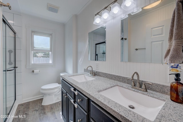 full bathroom featuring crown molding, toilet, a shower with shower door, and a sink