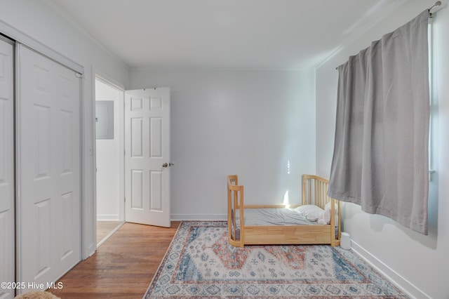 bedroom featuring electric panel, wood finished floors, baseboards, and ornamental molding
