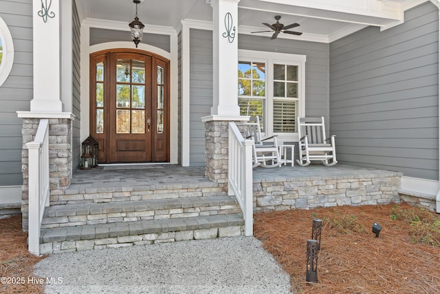 view of exterior entry with stone siding, covered porch, and ceiling fan