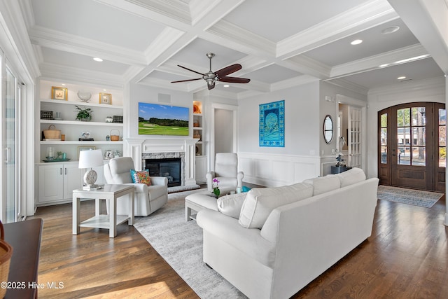 living area featuring dark wood-type flooring, coffered ceiling, built in features, beamed ceiling, and a glass covered fireplace