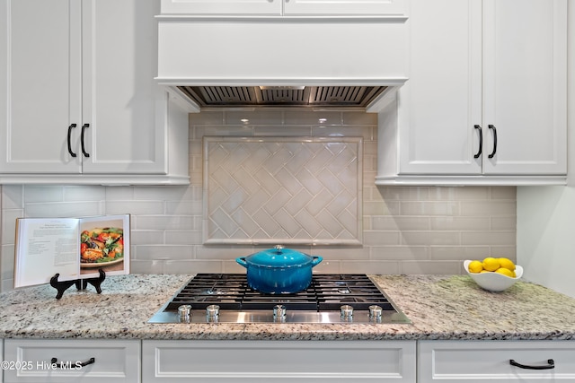 kitchen with premium range hood, stainless steel gas stovetop, white cabinets, and backsplash