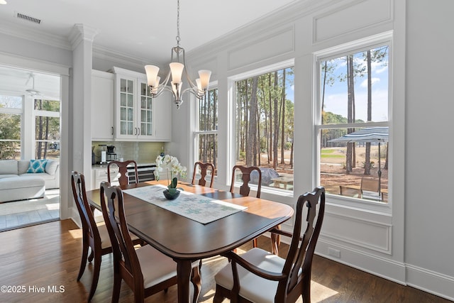 dining area with dark wood finished floors, crown molding, visible vents, a decorative wall, and a chandelier