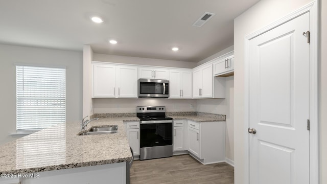 kitchen featuring light stone counters, appliances with stainless steel finishes, white cabinets, and a sink