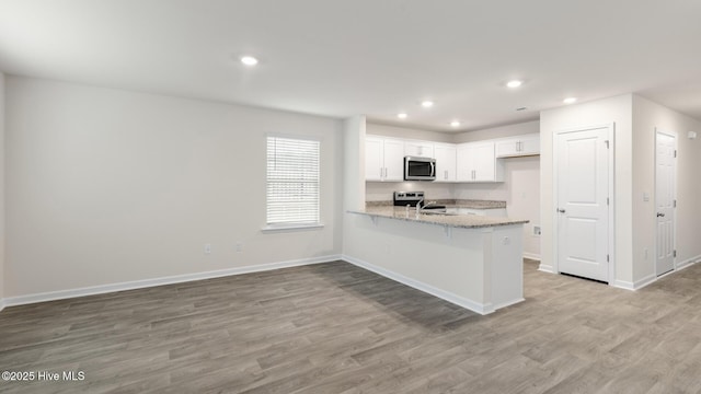 kitchen featuring light wood finished floors, a peninsula, light stone countertops, stainless steel appliances, and white cabinetry