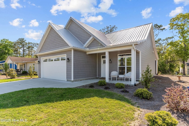 view of front of property with covered porch, an attached garage, metal roof, driveway, and a front lawn