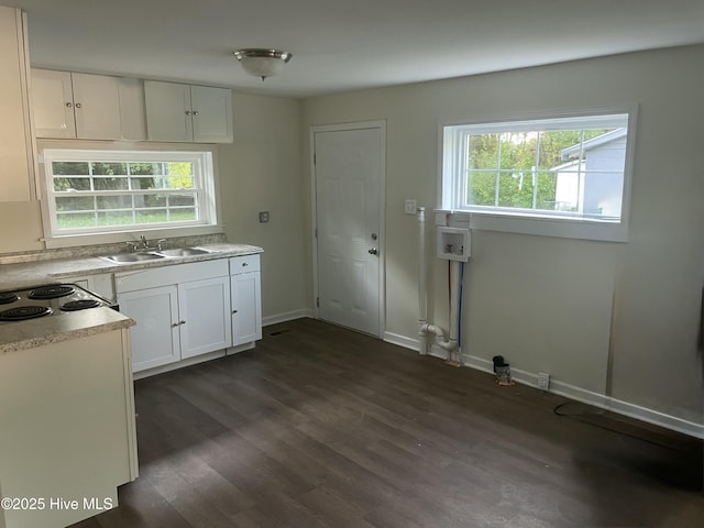 kitchen with light countertops, dark wood-type flooring, white cabinetry, a sink, and baseboards