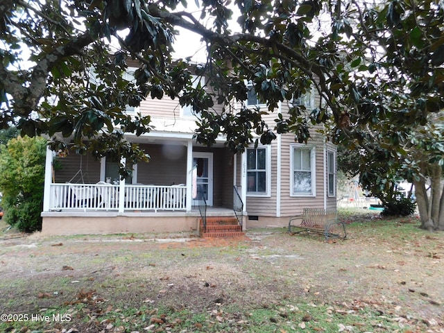 view of property hidden behind natural elements featuring crawl space and covered porch