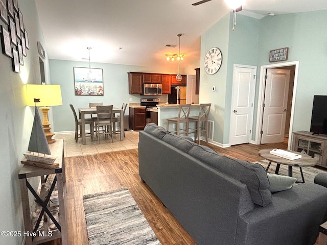 living room with a ceiling fan, light wood-type flooring, high vaulted ceiling, and baseboards