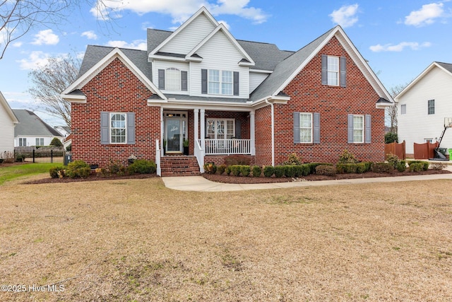 view of front of house with brick siding, a porch, a front yard, and roof with shingles