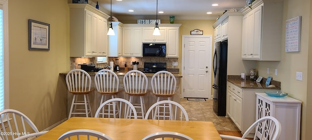 kitchen featuring decorative light fixtures, a breakfast bar area, tasteful backsplash, white cabinetry, and black appliances
