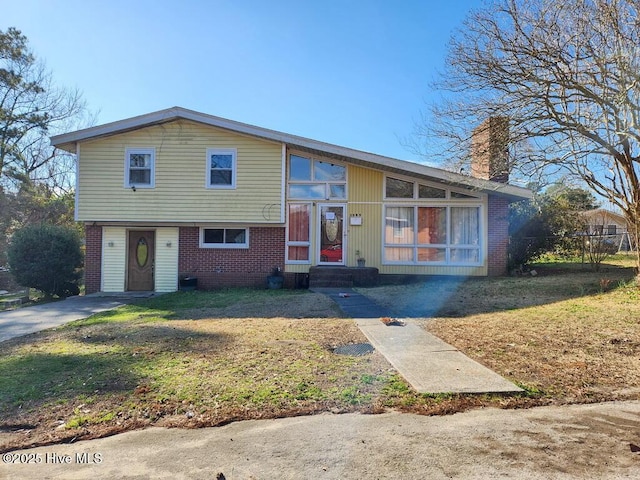 view of front of home with entry steps, a front yard, a chimney, and brick siding