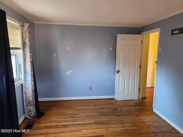 empty room with ornamental molding, visible vents, baseboards, and wood finished floors