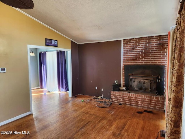 unfurnished living room featuring lofted ceiling, a textured ceiling, a brick fireplace, and wood finished floors