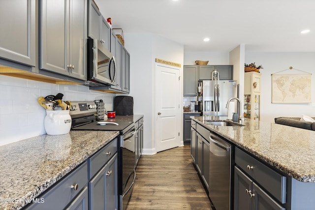 kitchen with light stone counters, dark wood-type flooring, stainless steel appliances, a sink, and recessed lighting