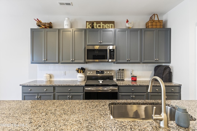 kitchen with gray cabinetry, stainless steel appliances, a sink, visible vents, and backsplash