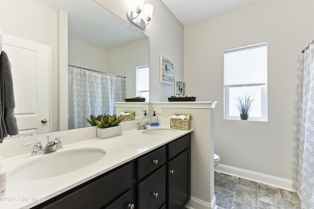 bathroom with toilet, double vanity, baseboards, and a sink