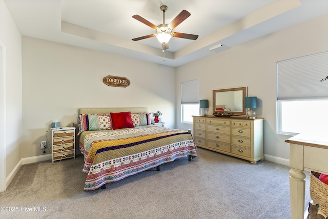 carpeted bedroom featuring a tray ceiling, a ceiling fan, and baseboards