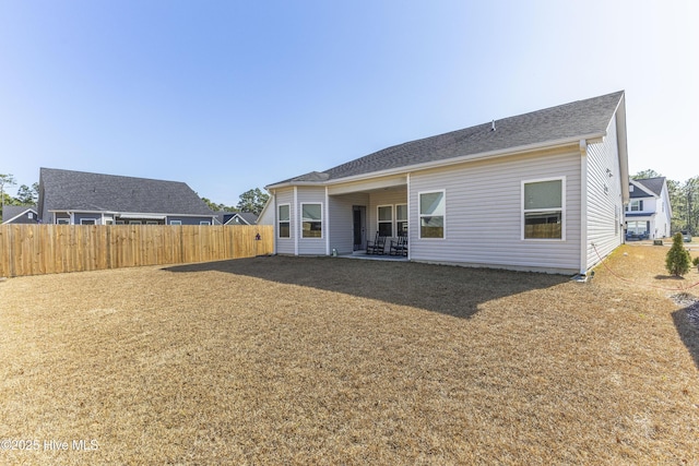 rear view of house with roof with shingles, fence, a patio, and a yard