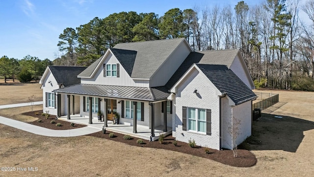 modern farmhouse featuring a porch, metal roof, a standing seam roof, a front lawn, and brick siding