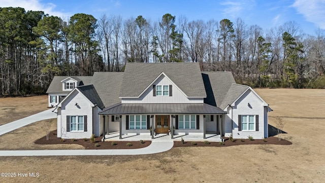 view of front of house with a porch, metal roof, roof with shingles, a standing seam roof, and a front lawn