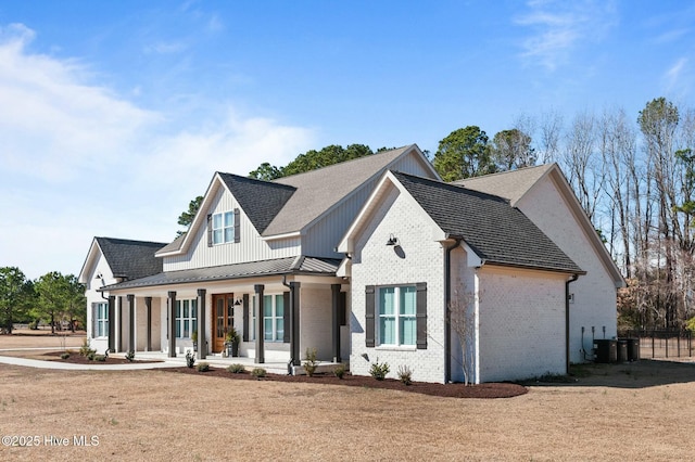 modern farmhouse featuring brick siding, a standing seam roof, a porch, central AC, and a front yard