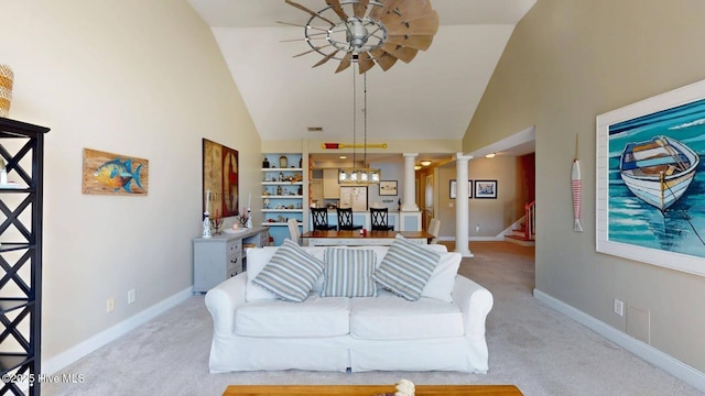 carpeted living area with high vaulted ceiling, a ceiling fan, baseboards, stairs, and ornate columns