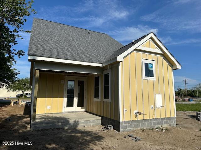 back of house featuring board and batten siding, a shingled roof, and french doors