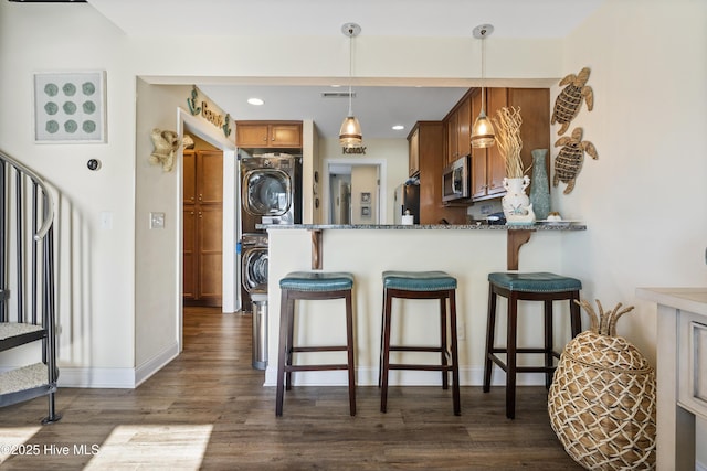 886 New River Inlet Rd Unit 41, North Topsail Beach, NC 28460 - kitchen featuring stainless steel microwave, stacked washer and clothes dryer, brown cabinetry, freestanding refrigerator, and dark wood-style floors